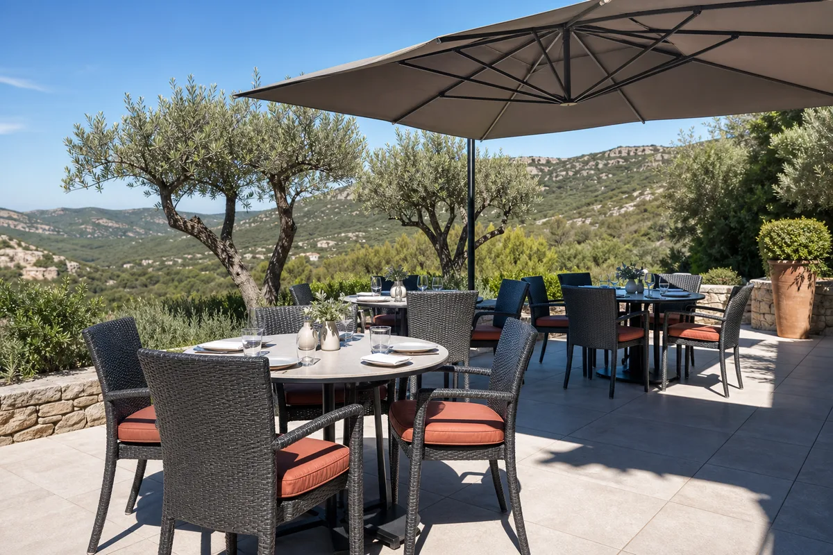 Terrasse extérieure ombragée avec tables et chaises en résine tressée grise face à la garrigue