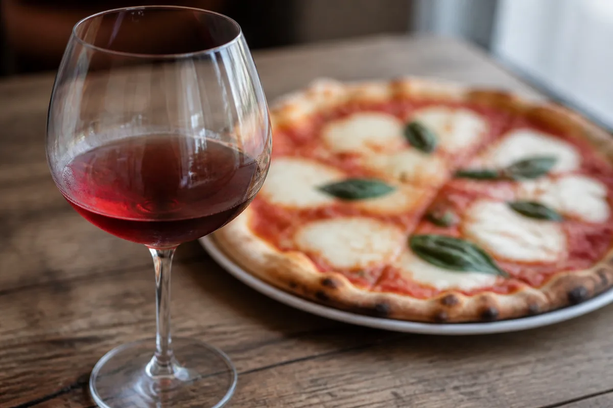 Verre de vin rouge posé près d&rsquo;une pizza margherita sur une table en bois