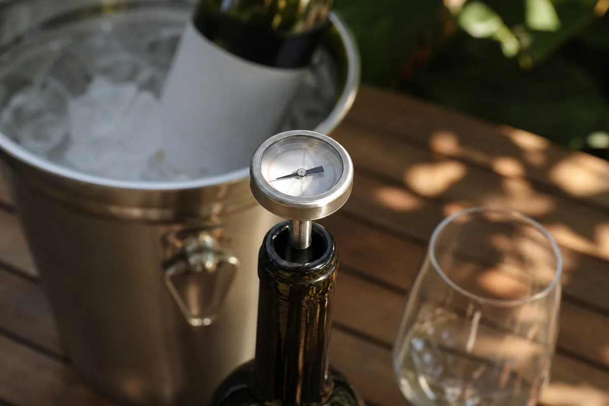 Thermomètre à vin plongé dans le col d&rsquo;une bouteille sur une table de terrasse ombragée