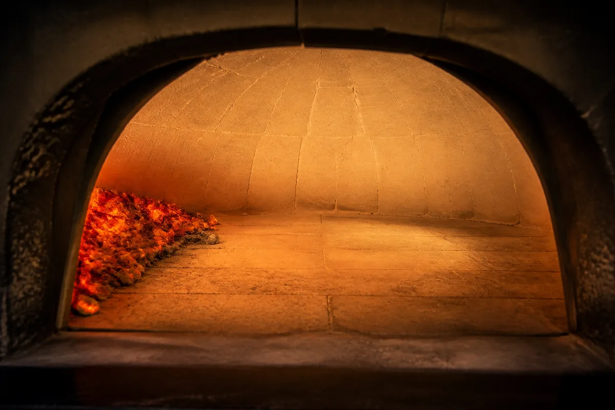 Intérieur d&rsquo;un four à pizza en briques réfractaires, voûte blanchie et lit de braises rougeoyantes sur le côté